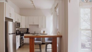 Une cuisine moderne avec des armoires blanches, des appareils en acier inoxydable et un îlot central en bois doté de tabourets de bar.