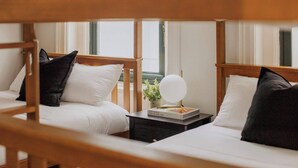 Une chambre d’hôtel avec deux lits, chacun étant équipé de draps blancs et d’oreillers noirs. On y trouve une petite table avec un livre et un miroir rond placé entre les deux lits.