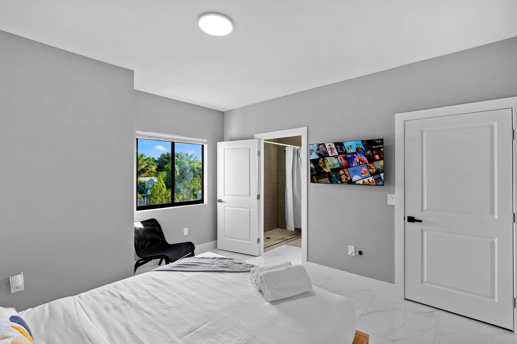 Camera moderna con un letto grande, una finestra vista sul verde, zona doccia e TV a parete.