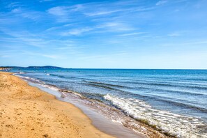 A beach with clear blue water, sandy shore, and distant hills.