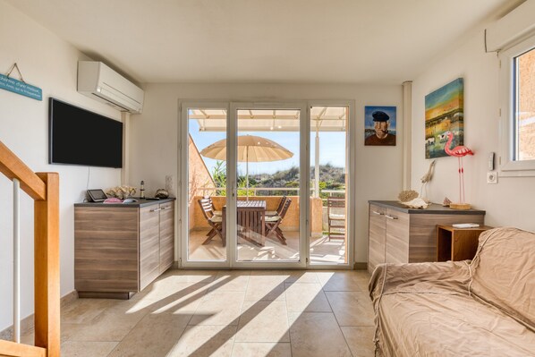 A modern room with a sliding glass door to a balcony, a flat-screen TV, a wooden dining table, and a bed.