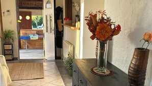 A hallway with a tiled floor, a black console table with a vase of flowers, a wooden bench, and a view into a room with a wooden ceiling and a door.