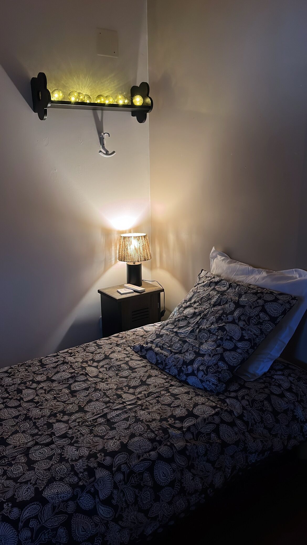 Un dormitorio con una cama, una lámpara de noche, un aplique de pared y una mesita de noche.