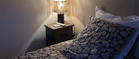 Un dormitorio con una cama, una lámpara de noche, un aplique de pared y una mesita de noche.