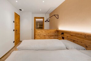 Un dormitorio con cabecera de madera, una cama con ropa de cama blanca, una puerta de madera y una lámpara fijada a la pared.