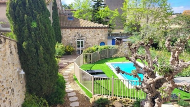 Ein Steinhaus mit Schwimmbad, umgeben von einem Garten und einem hohen Baum.