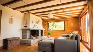 A cozy living room with a stone fireplace, wooden beams, a sofa, and a large window. - Stay in the heart of the Gaschney 360° resort (Muhlbach-sur-Munster)