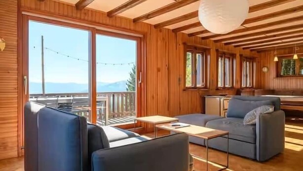A wooden interior with a sofa, a small table, and a view through large windows. - Stay in the heart of the Gaschney 360° resort (Muhlbach-sur-Munster)