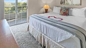 A bedroom with a bed, a nightstand, a lamp, a painting, and a view through a sliding door.