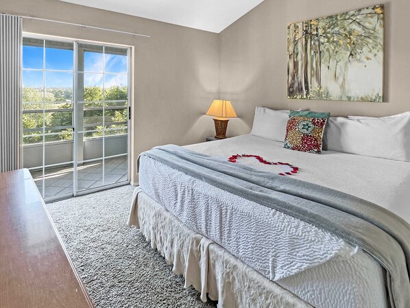 Une chambre à coucher avec un lit, une table de chevet, une lampe, un tableau et une vue sur l’extérieur, visible à travers une porte coulissante.