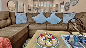 A living room with a brown leather sofa, decorative pillows, a coffee table with a fruit tart, and wall art.