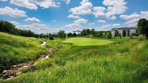 A golf course with a stream, trees, and buildings in the background.