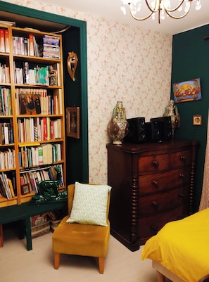 A room with a bookshelf, a wooden dresser, a green armchair, and a yellow bed.