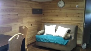 A room with wooden walls, a sofa with pillows, a chair, a clock, and a table. - In the midst of wildlife and marshland, a ton of thrills and chills  (Vendays-Montalivet)