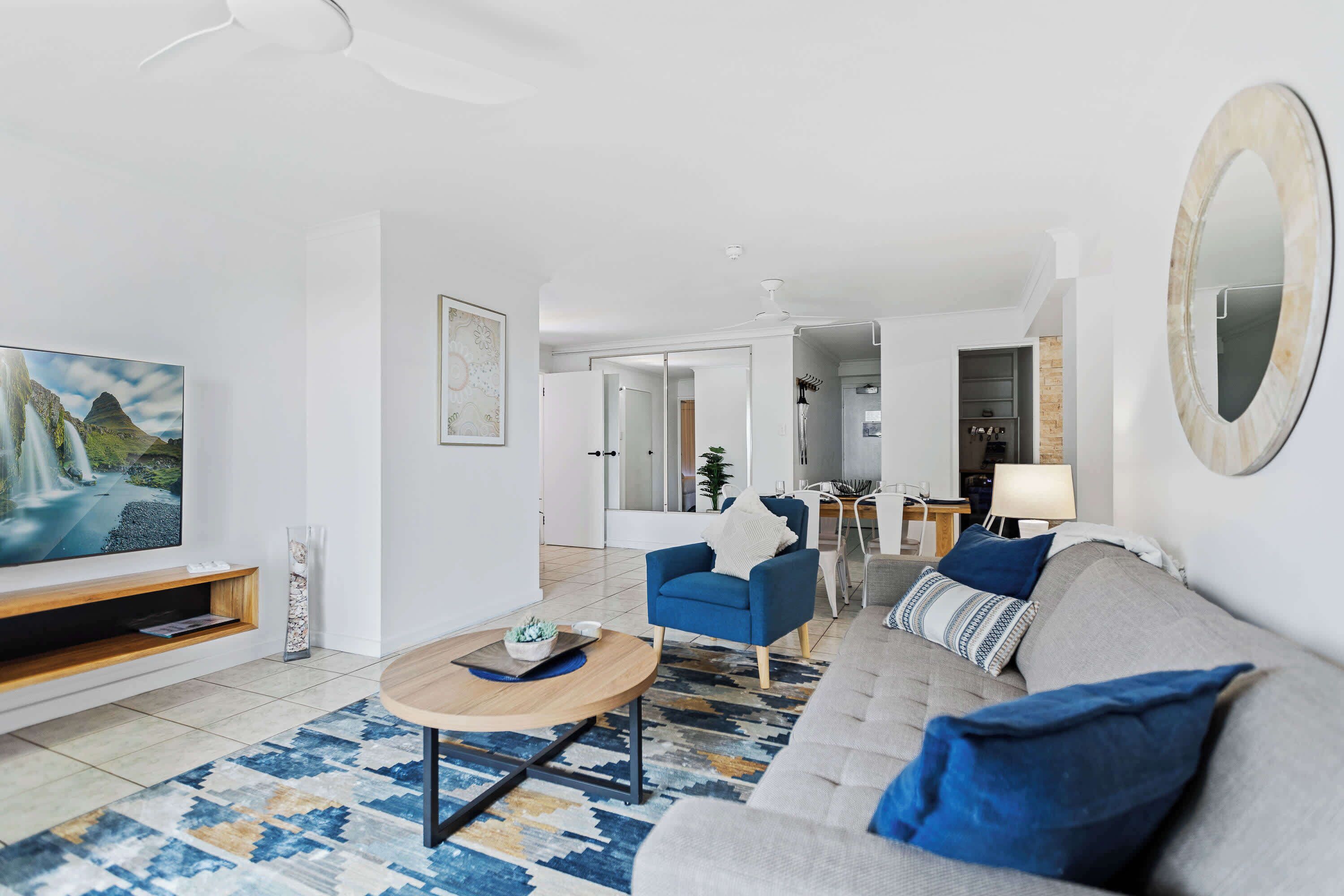 Una sala de estar moderna con un sofá, una mesa de centro, un televisor y un sillón azul.