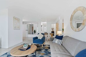 A modern living room with a sofa, armchair, coffee table, and a dining area in the background.