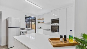 A modern kitchen with white cabinetry, a large island, a refrigerator, an oven, and a sink.