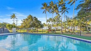 A clear blue pool surrounded by palm trees and a well-maintained lawn.