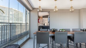 Et moderne spiseområde med et træbord og fletstole, store vinduer med udsigt over byen samt hængende pendellamper.