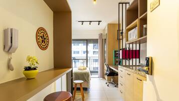 Quarto de hotel compacto com cozinha compacta, cama com vista, um banquinho pequeno e uma planta em vaso.