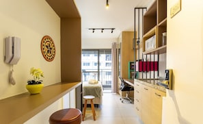 A compact hotel room with a kitchenette, a bed with a view, a small stool, and a potted plant. - THK - Building With Pool in the Republica Neighborhood in SP (São Paulo)