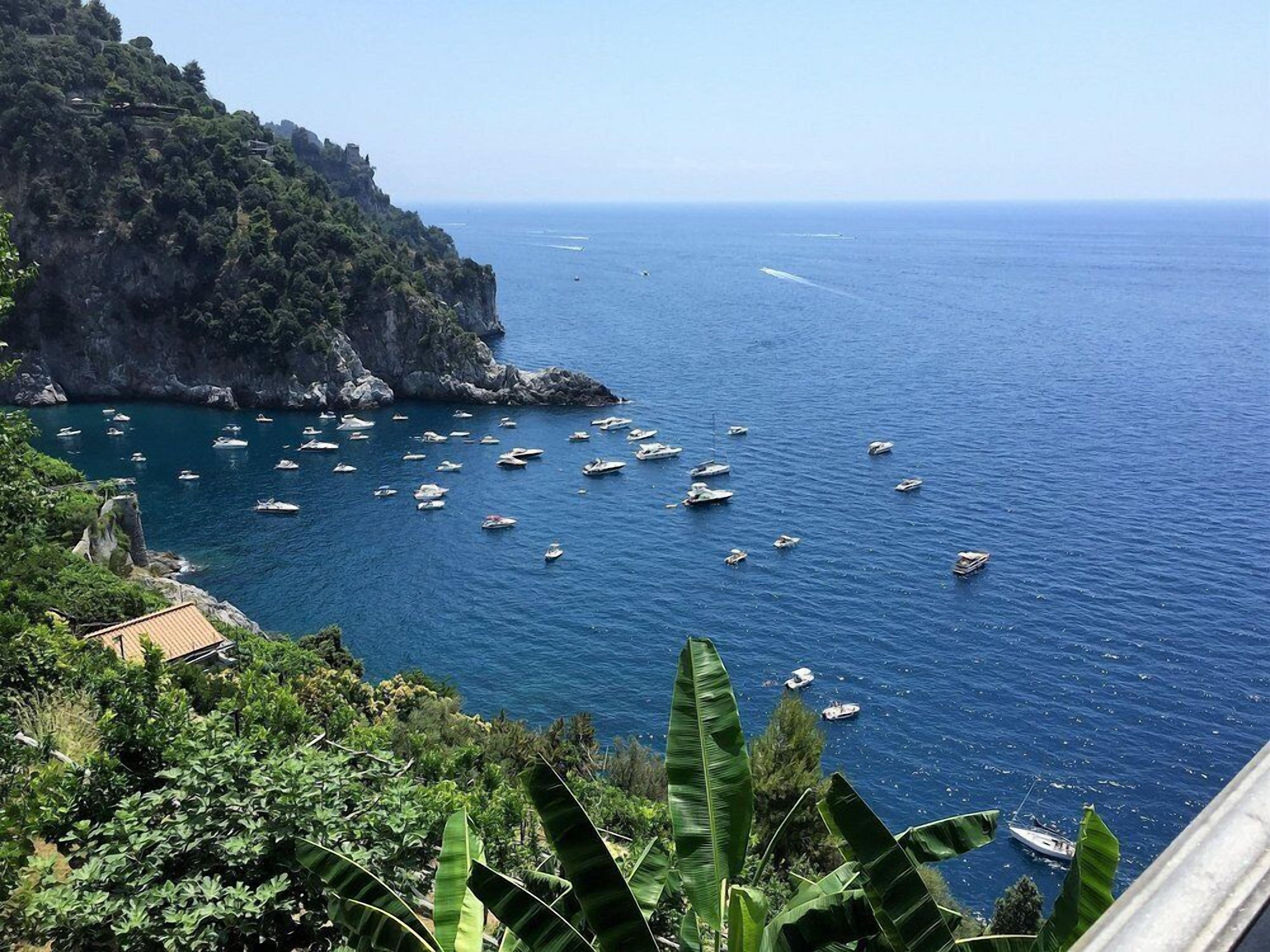 Vista costera con barcos en el agua y montañas al fondo.