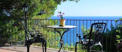 Une terrasse avec deux chaises en métal et une petite table ronde, un pot de fleurs et une lampe.