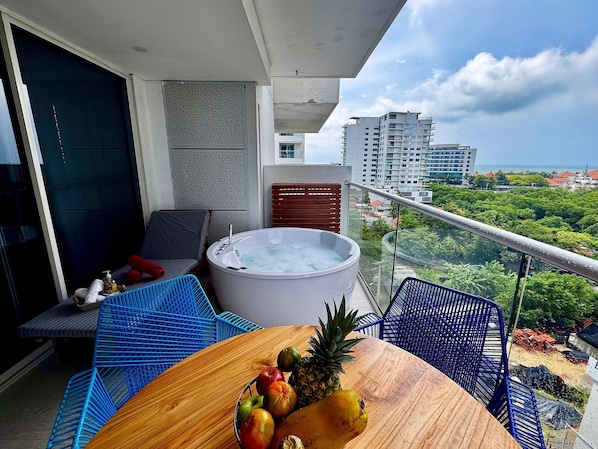 A balcony with a hot tub, blue chairs, a wooden table with fruits, and a city view. - 808 Martinique (Cartagena)