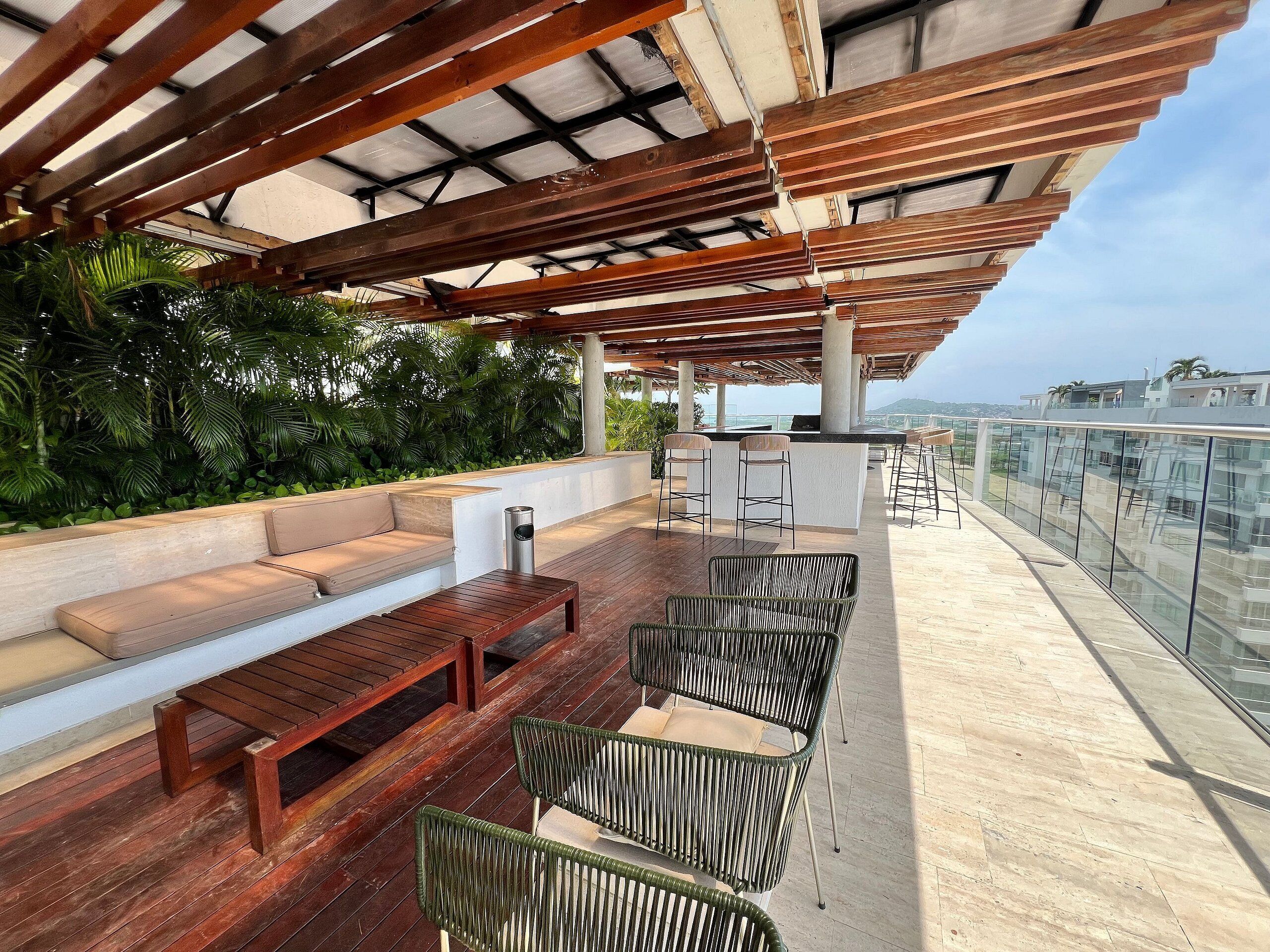A covered outdoor seating area with wooden furniture and a bar.