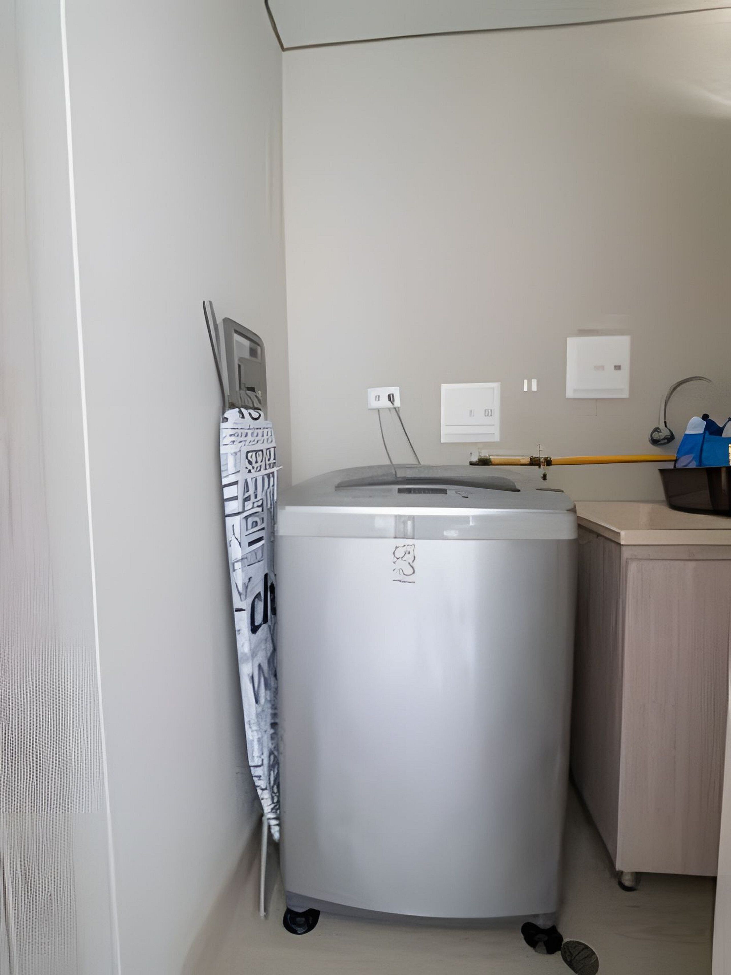 A compact, modern bathroom with a grey washing machine, a small wooden cabinet, and a towel rack with a patterned towel.