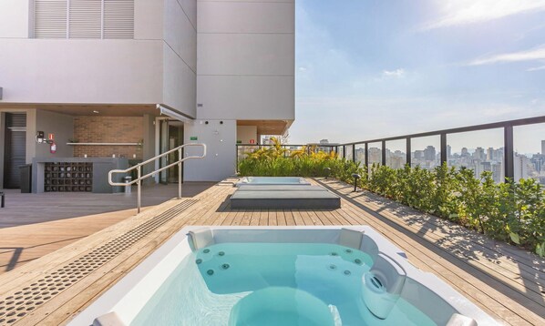Eine Dachterrasse mit Whirlpools, einer Bar und Blick auf die Stadt.