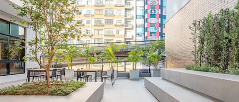 Un espace extérieur aménagé en terrasse, avec des sièges et des jardinières, entouré d’immeubles.