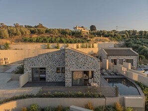 A stone building with a pool and outdoor seating, surrounded by greenery and a hillside in the background.