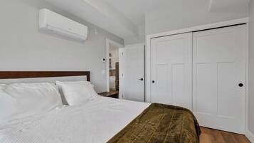 A bedroom with a bed, white walls, a wooden headboard, a brown throw blanket, and white doors.