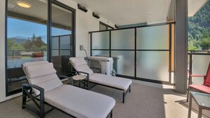 A balcony with two lounge chairs, a table, and a view of mountains. - Harrison Hot Springs Lakeside. One Bedroom Apartment, Balcony and Mountain View. (Harrison Hot Springs)