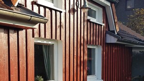 Ein rotes Holzhaus mit zwei Fenstern, eines mit Vorhang, eines geöffnet.