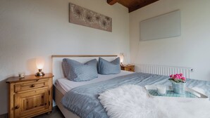 A bedroom with a wooden headboard, a bedside table with a lamp, a nightstand, a bed with patterned bedding, a decorative wall piece, and a tray with a flower vase.