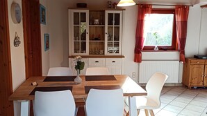 Ein Essbereich mit einem Holztisch, weißen Stühlen, einer Vitrine und einem Fenster mit Vorhängen.