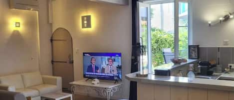 A modern living room with a flat-screen TV, a sofa, a coffee table, and a kitchen area with a counter and cabinets.