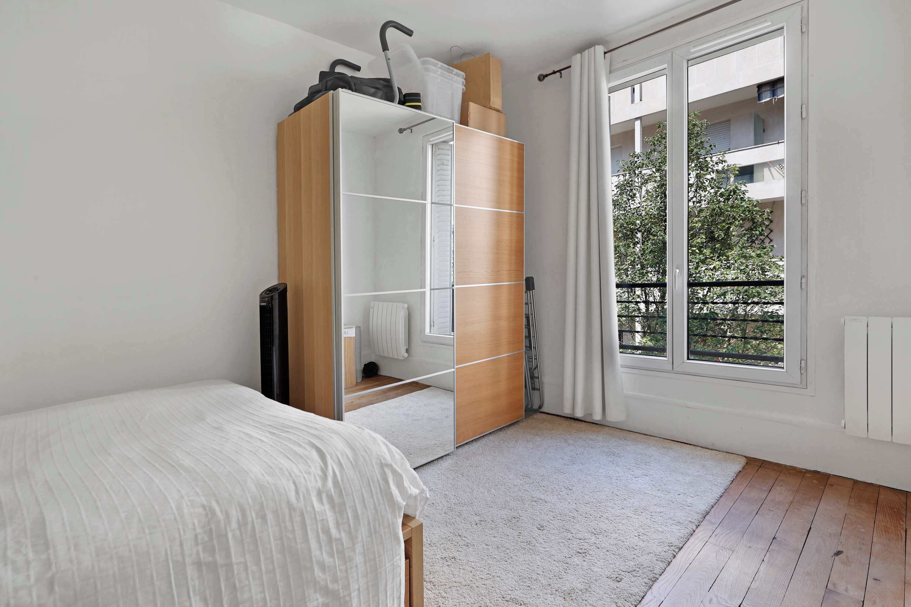 Une chambre à coucher comprenant un lit, une armoire, un miroir et une fenêtre donnant sur un balcon.