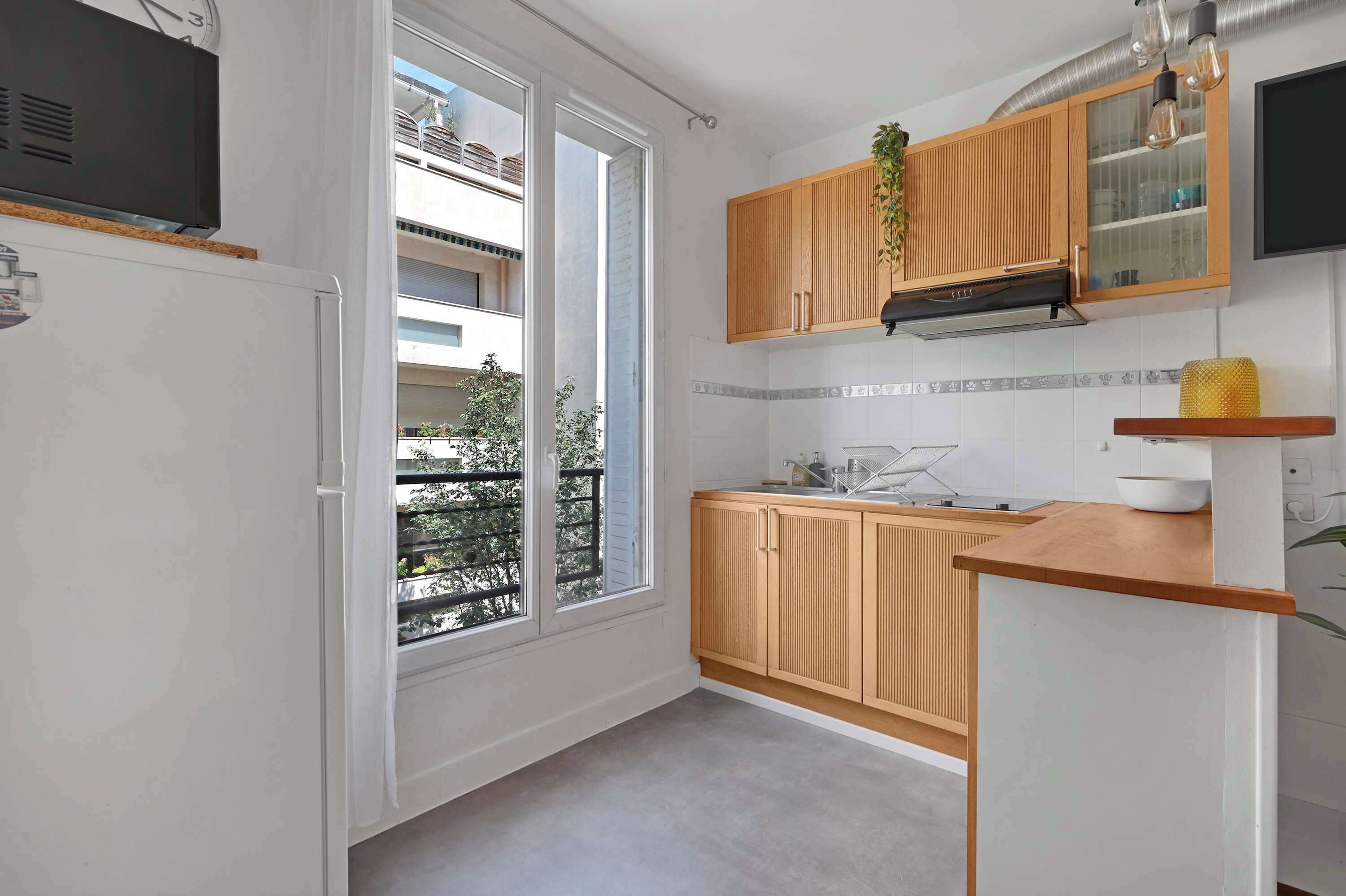Une cuisine moderne avec des meubles en bois, un four encastré et une grande fenêtre donnant sur le balcon.