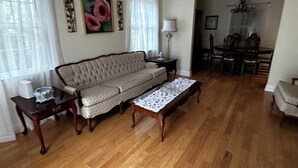 A living room with a sofa, a coffee table, and a dining area with a chandelier. - The Josephine  8 Beds (Fort Walton Beach)