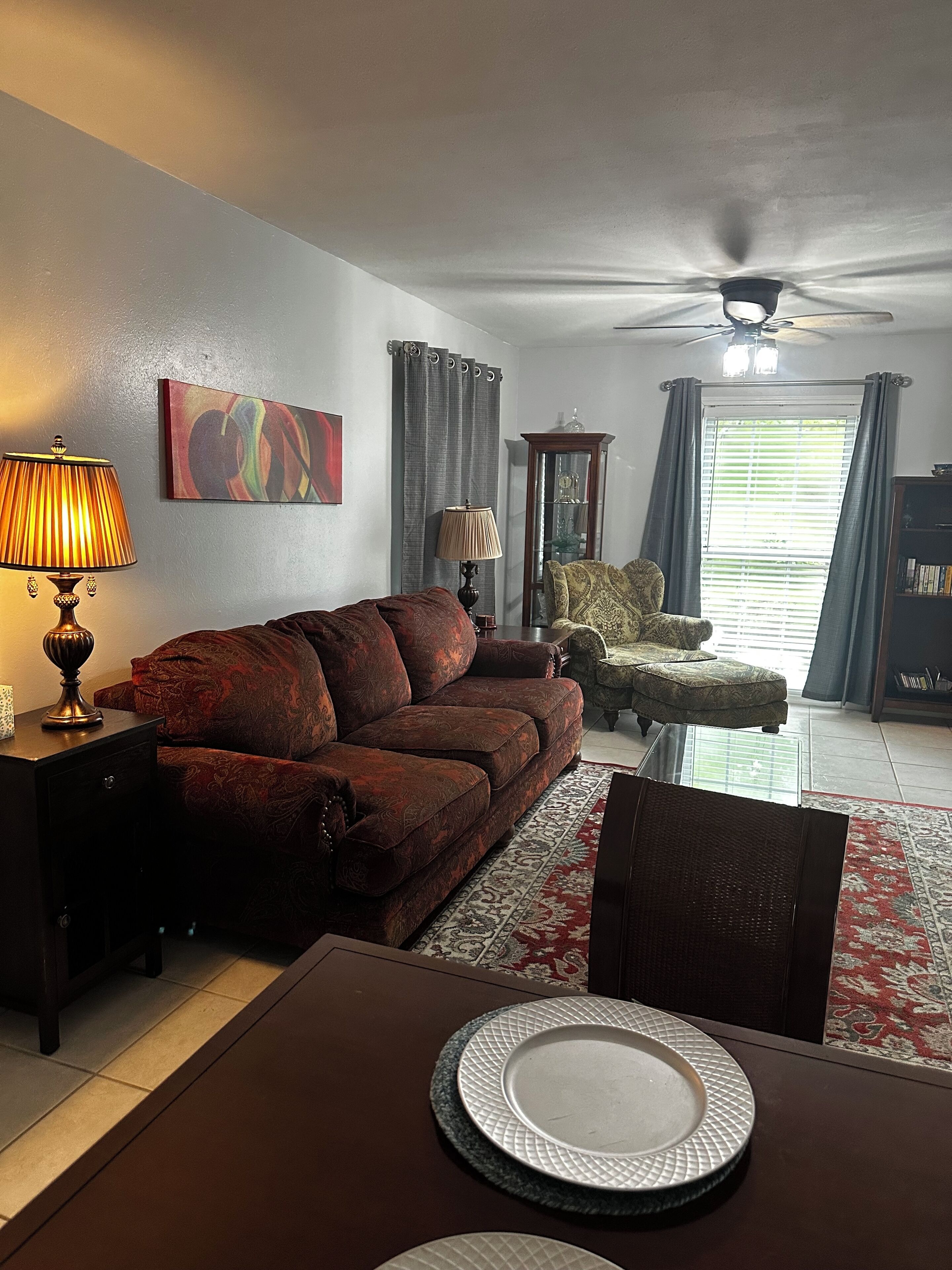 A living room with a sofa, a dining table with plates, a lamp, and a ceiling fan.