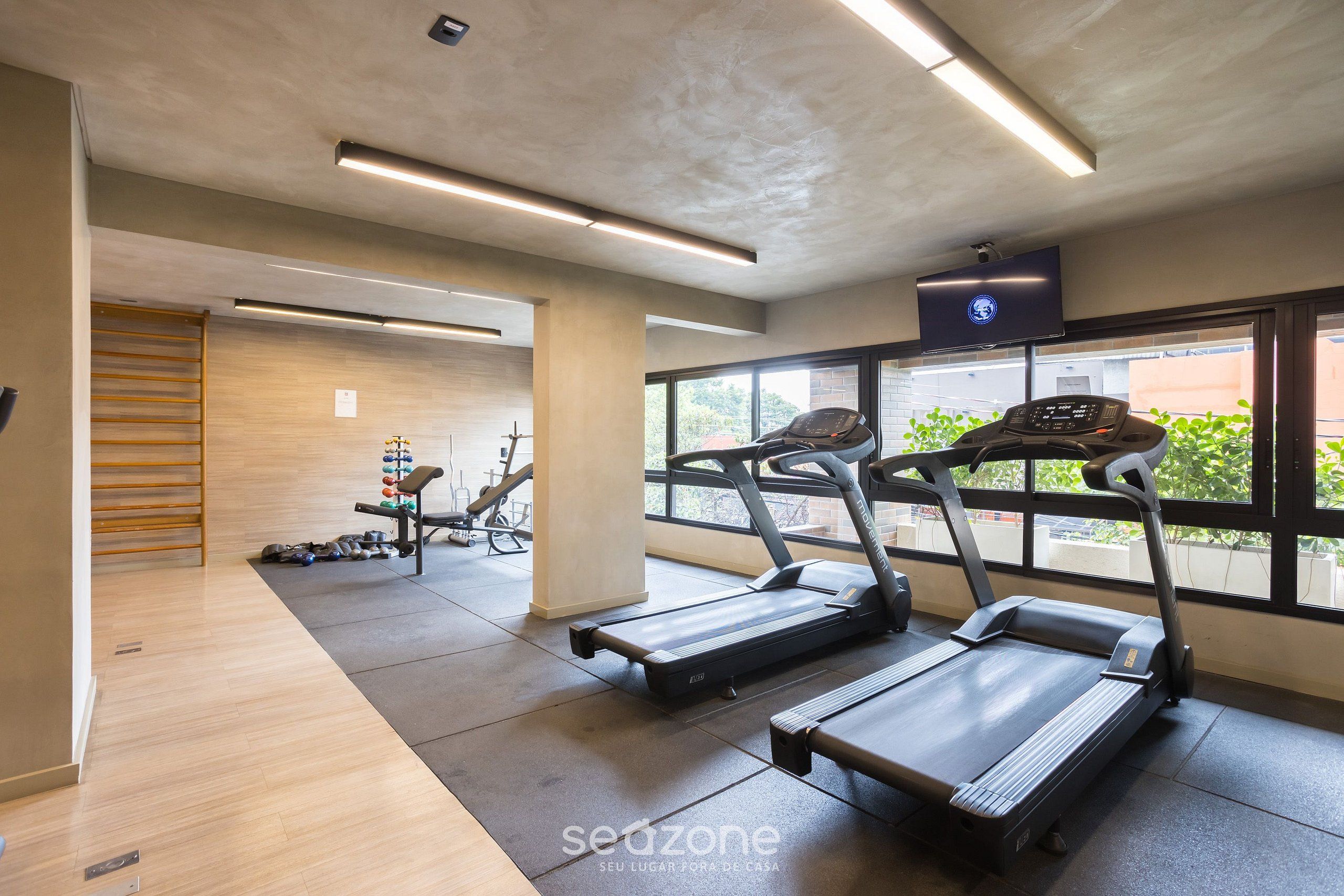 Une salle de sport moderne équipée de tapis de course, d’appareils de musculation et d’une grande fenêtre laissant entrer la lumière naturelle.