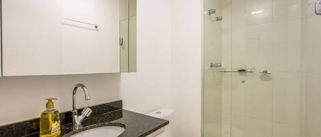A modern bathroom with a glass-enclosed shower, a white toilet, and a granite countertop with a soap dispenser.