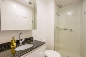 Een moderne badkamer met een glazen douchecabine, een wit toilet en een granieten aanrecht met een zeepdispenser.