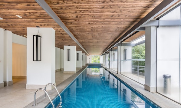 A modern indoor swimming pool with a wooden ceiling, clear glass walls, and a tiled floor. - Modern Studio 450m From the Subway Ism0806 (São Paulo)