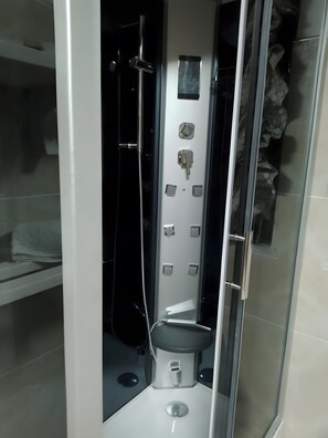 Un baño moderno con ducha de vidrio, inodoro y un estante pequeño con toallas.