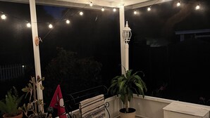 A covered outdoor area with string lights, potted plants, a bench, and a white cabinet.