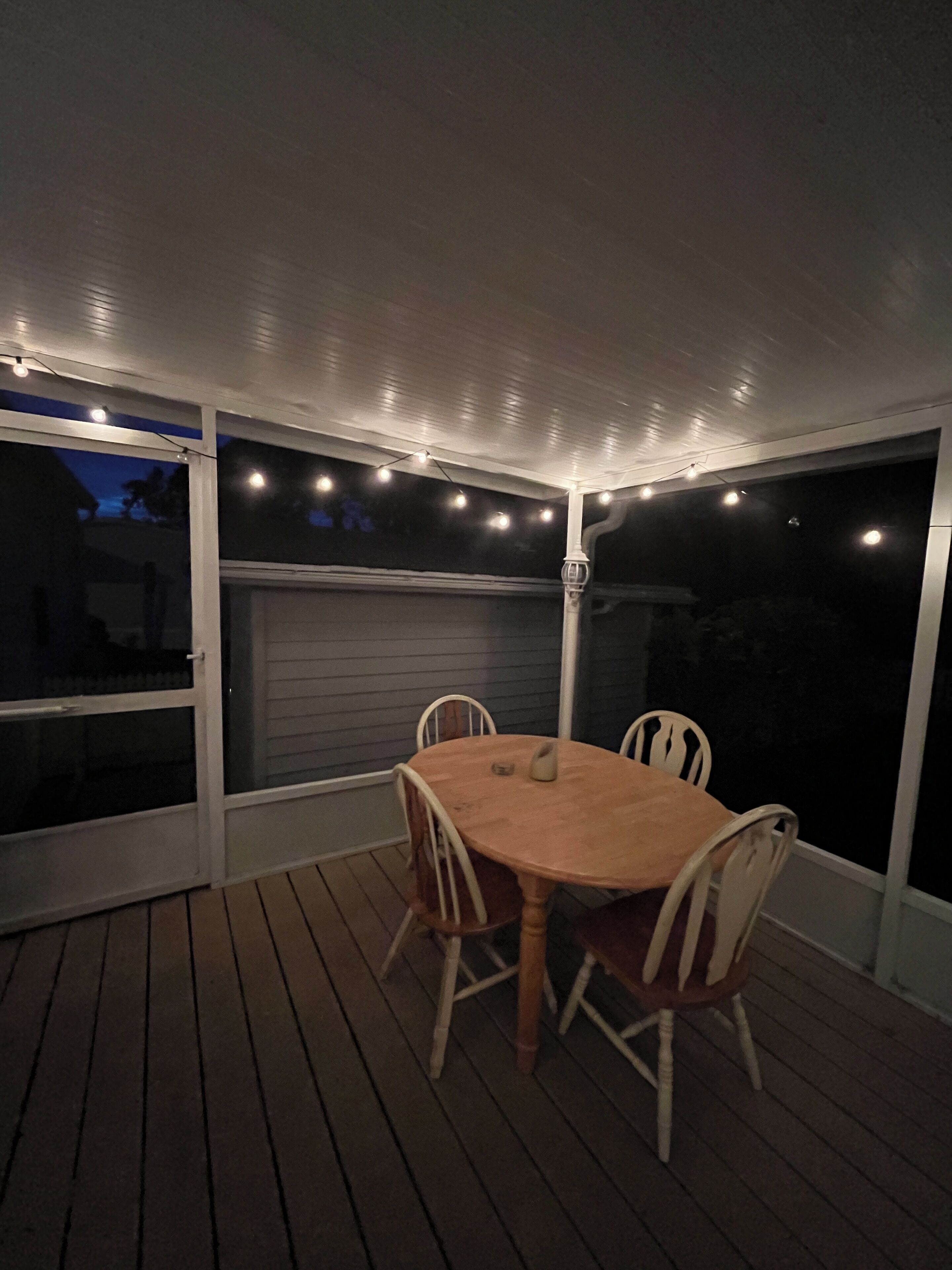 Eine Terrasse im Freien mit Holztisch und -stühlen, Lichterketten und einer Garagentür im Hintergrund.